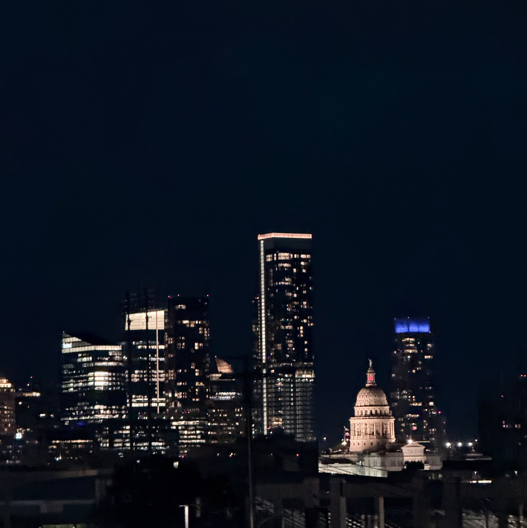 A city skyline at night features illuminated skyscrapers and a prominent domed building.
